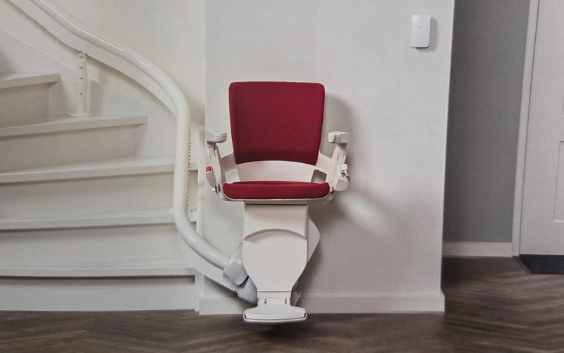 Montascale con poltroncina rossa fermo alla stazione bassa di una scala interna, con la guida curva che sale lungo i gradini
